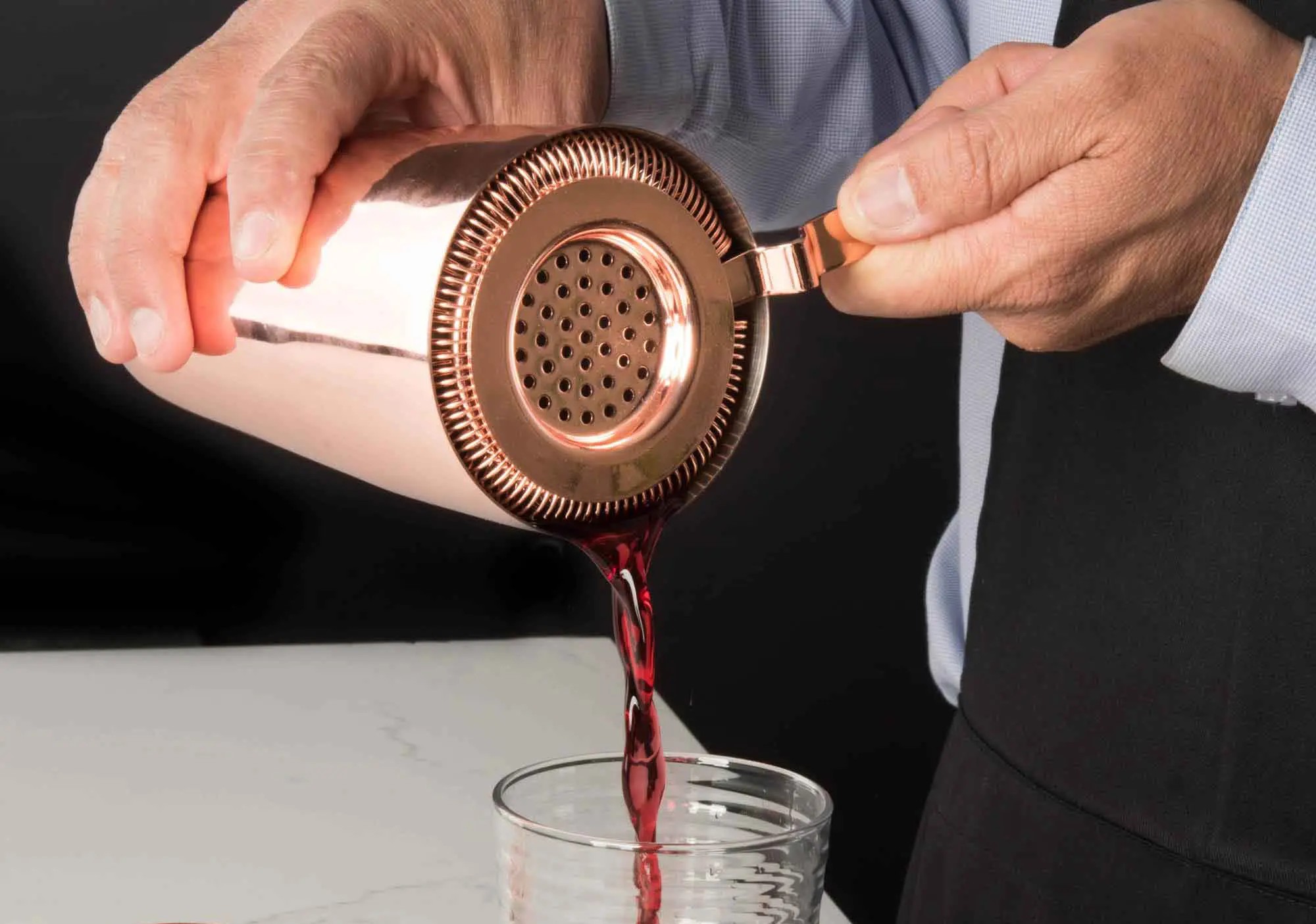 «تصویر استرینر استیل براق مخصوص بار سرد روی سطح چوبی، با طراحی فنری و سوراخدار، مناسب برای فیلتر کردن یخ و مواد جامد هنگام تهیه نوشیدنیهای خنک.»